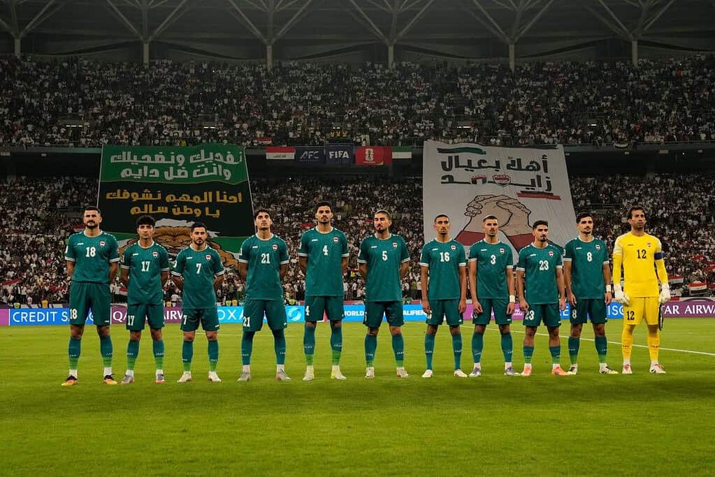 La selección de Irak formada antes de un partido de clasificación al Mundial 2026, con banderas y pancartas de hinchas al fondo