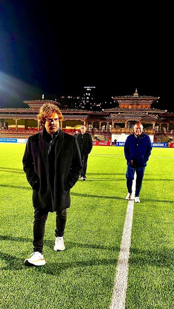 Rodolfo Zapata parado en el campo del Changlimithang Stadium de noche, con la arquitectura tradicional butanesa de fondo