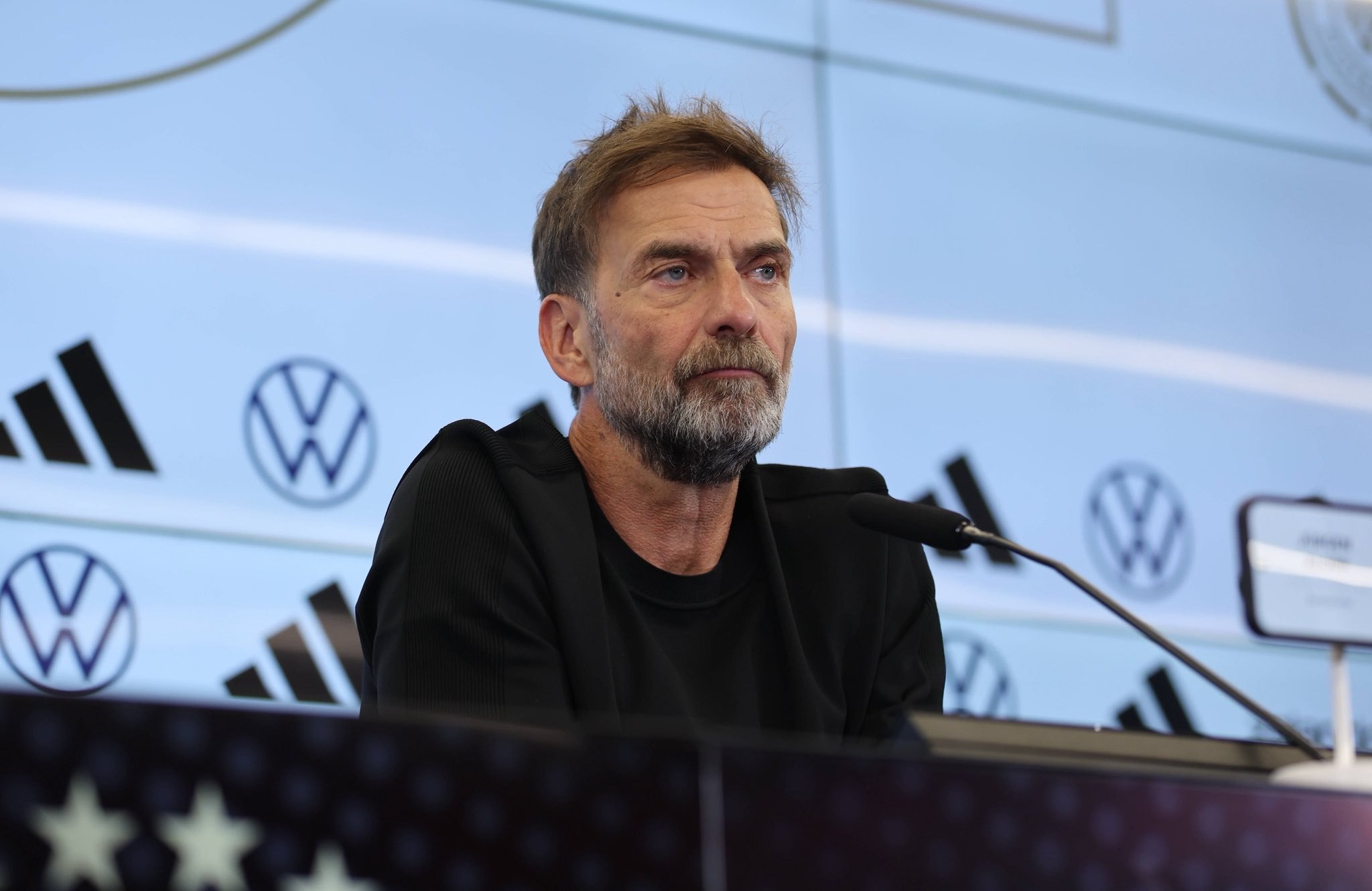 Jürgen Klopp sentado ante los micrófonos en la sala de prensa del DFB-Campus, con el fondo de patrocinadores de la selección alemana