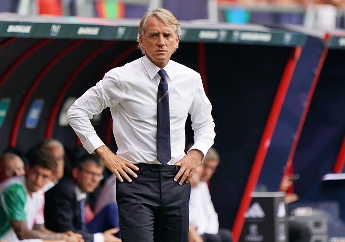 Roberto Mancini de camisa blanca y corbata oscura, con las manos en la cintura, parado al costado del campo frente al banco de suplentes