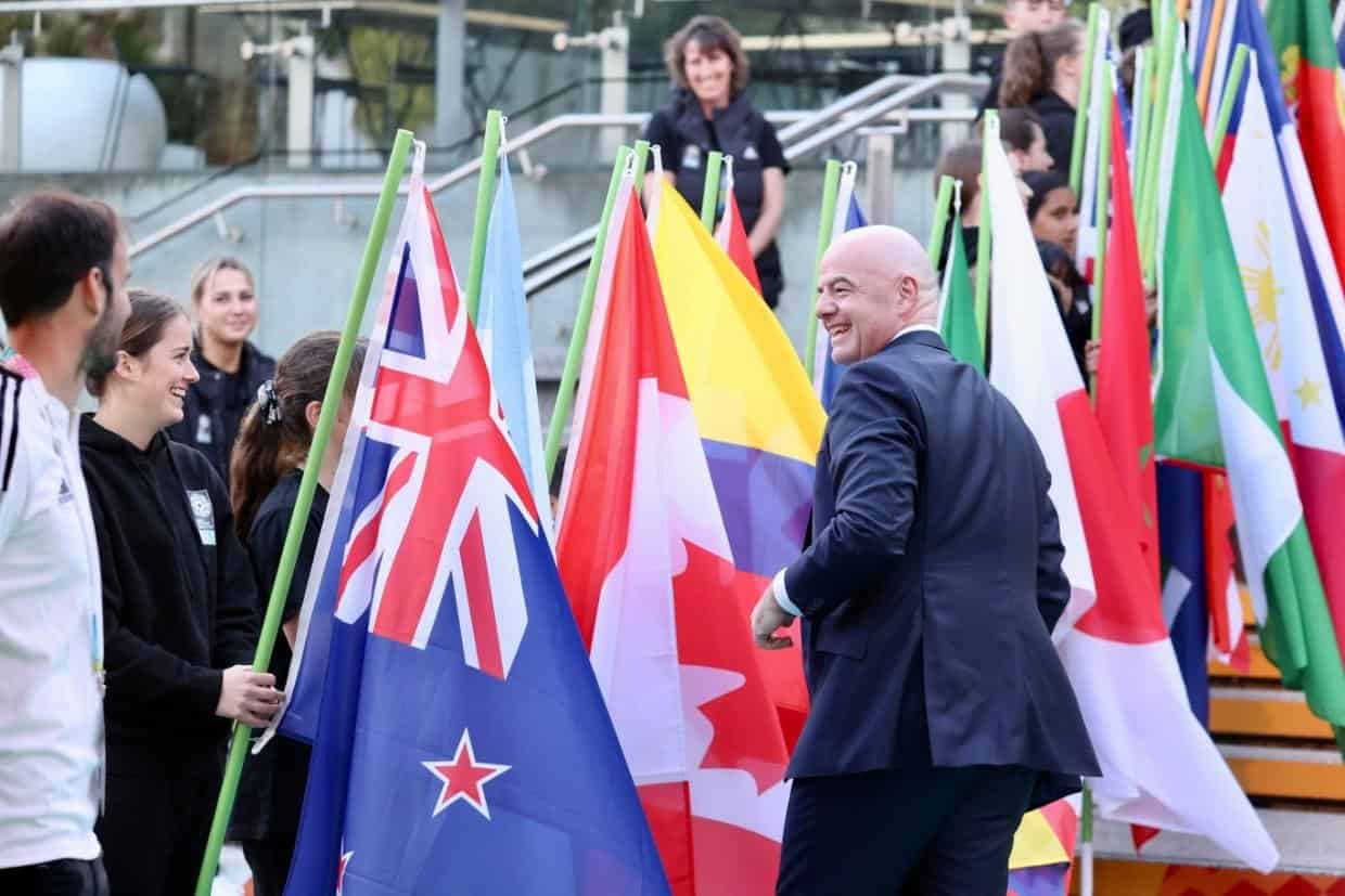 Gianni Infantino sonríe al pasar junto a una niña que sostiene la bandera de Nueva Zelanda en una ceremonia de la FIFA