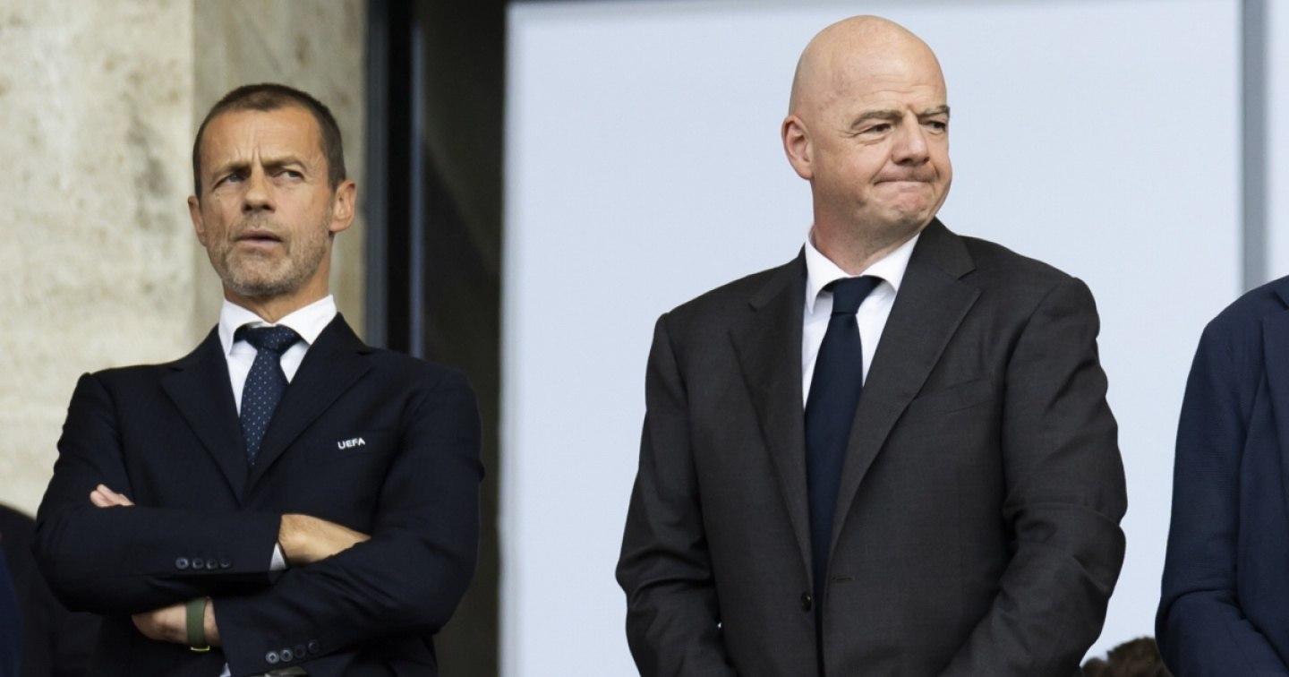 Aleksander Ceferin, de brazos cruzados, y Gianni Infantino, con gesto de incomodidad, de pie y de traje en un palco