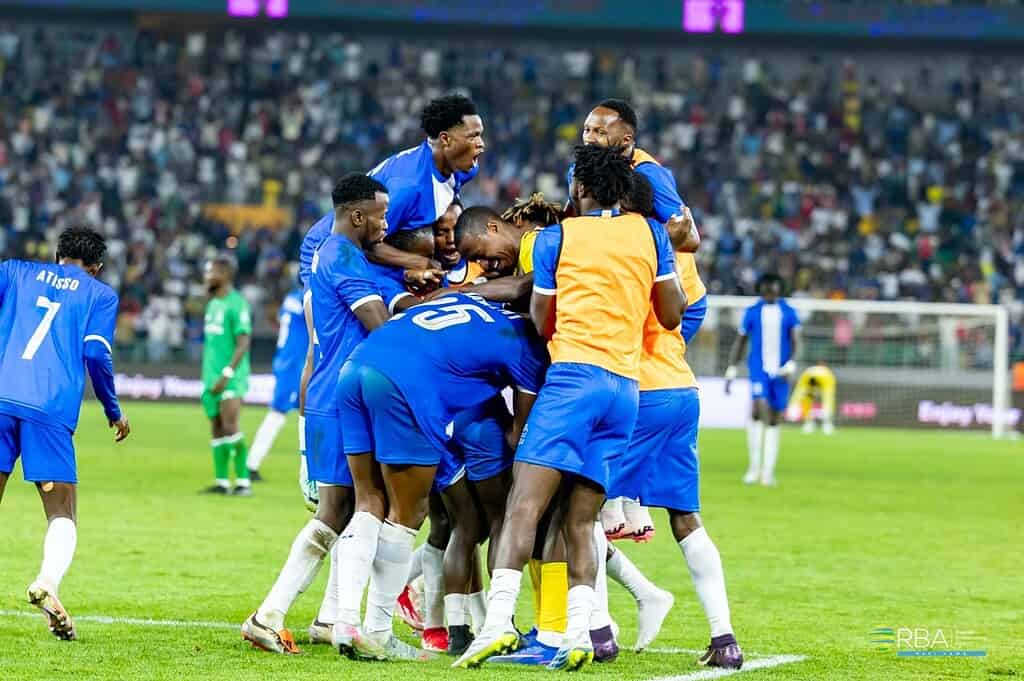 Jugadores de Rayon Sport se abrazan para festejar un gol en el Amahoro Stadium de Kigali, con las tribunas llenas y un futbolista de Gor Mahia de verde al fondo