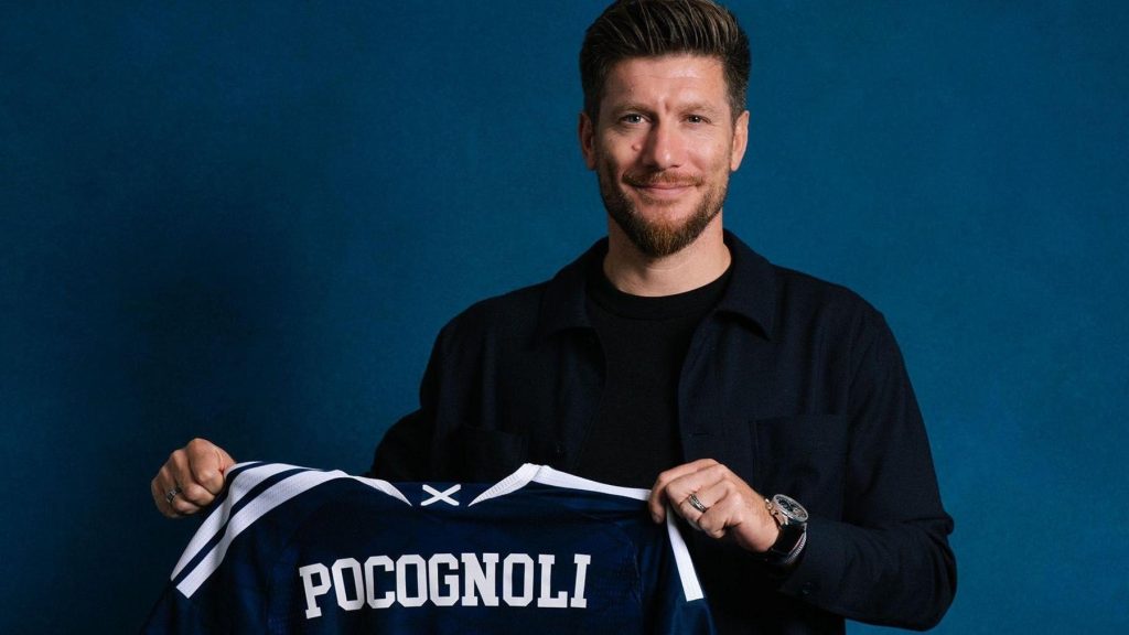 Sebastien Pocognoli sonrie mientras sostiene una camiseta azul de la seleccion de Escocia con su apellido estampado en la espalda