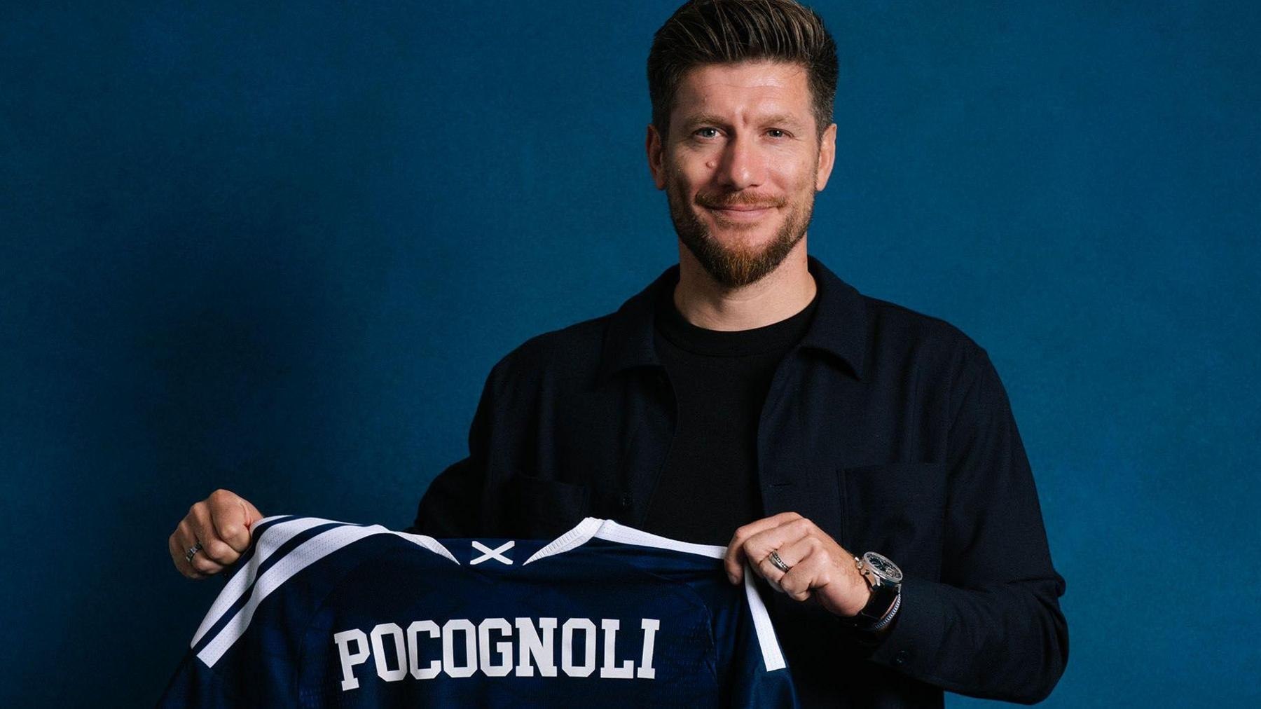 Sebastien Pocognoli sonrie mientras sostiene una camiseta azul de la seleccion de Escocia con su apellido estampado en la espalda
