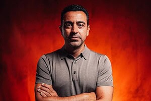 Xavi Hernández, de brazos cruzados y con remera gris, en un retrato sobre fondo rojo