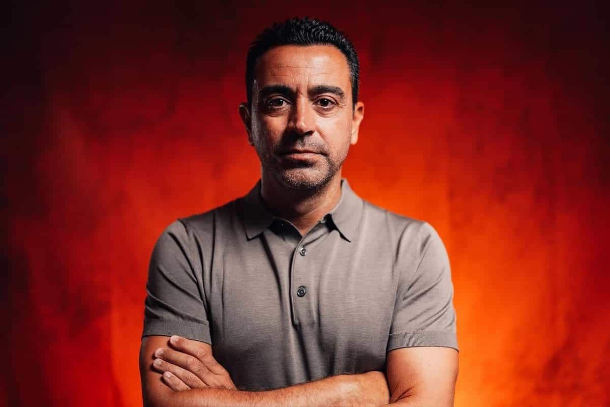 Xavi Hernández, de brazos cruzados y con remera gris, en un retrato sobre fondo rojo