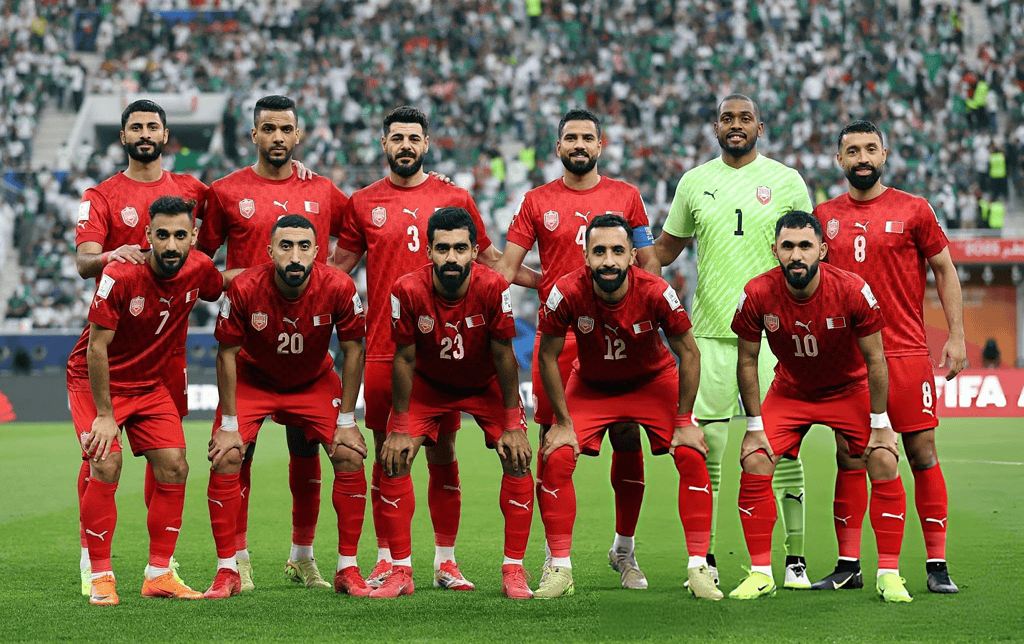 Jugadores de la selección de Bahréin posan con la camiseta roja antes de un partido en un estadio lleno