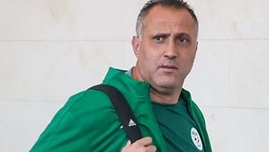 Brahim Hemdani con la campera verde de la selección argelina y un bolso al hombro, mirando a cámara frente a una pared blanca