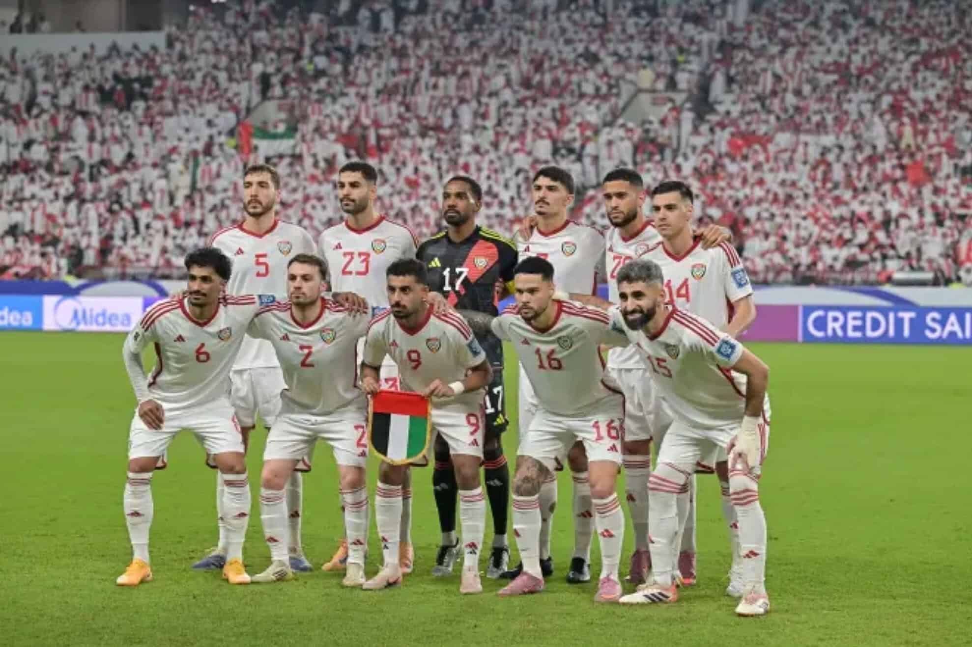 Los once titulares de la selección de Emiratos Árabes Unidos posan para la foto grupal antes de un partido, con camiseta blanca y la tribuna llena de fondo