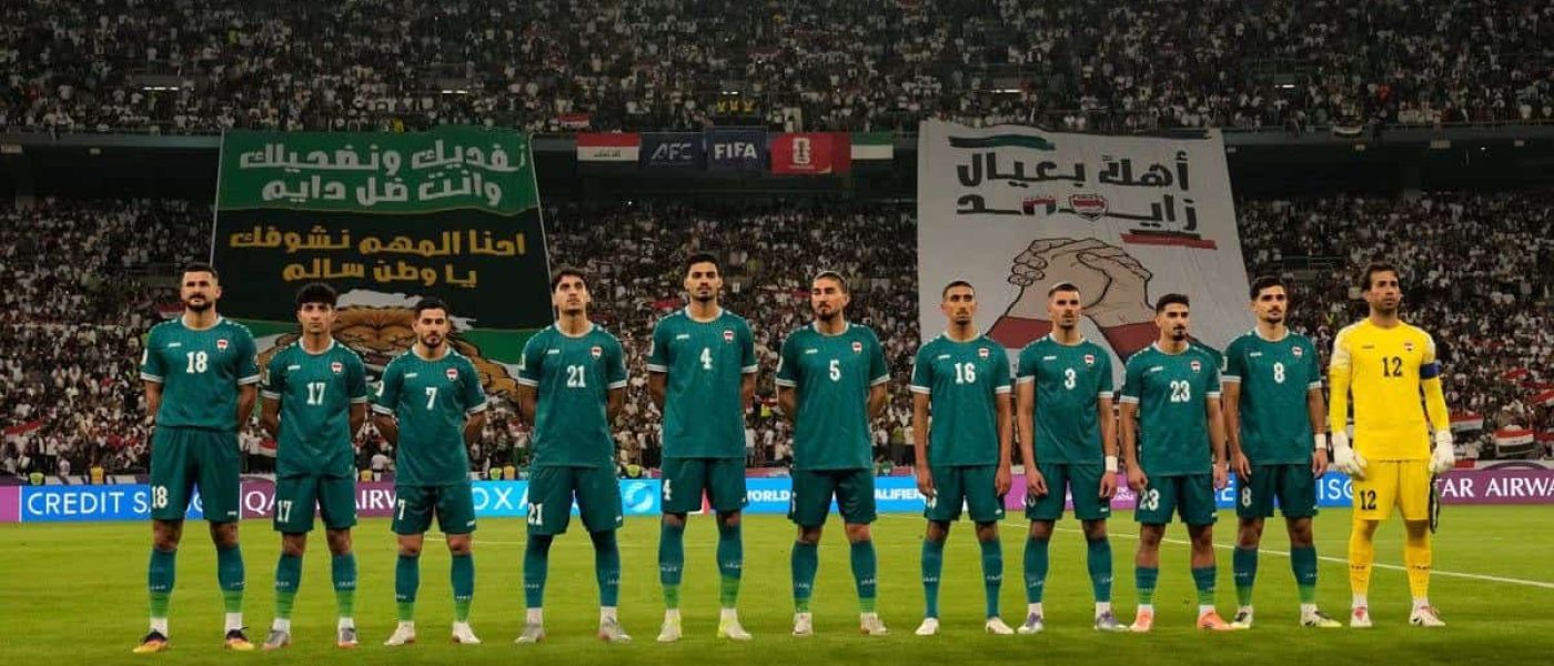 La selección de Irak formada antes de un partido de clasificación al Mundial 2026, con banderas y pancartas de hinchas al fondo