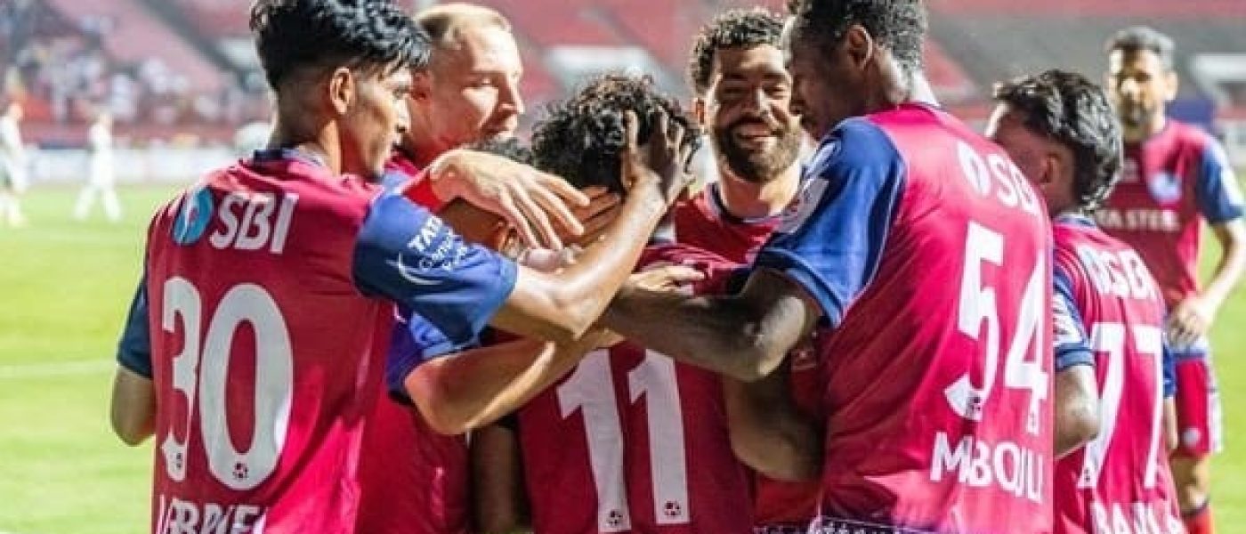 Jugadores de Jamshedpur FC se abrazan para festejar un gol con la camiseta roja y azul con el sponsor Tata Steel