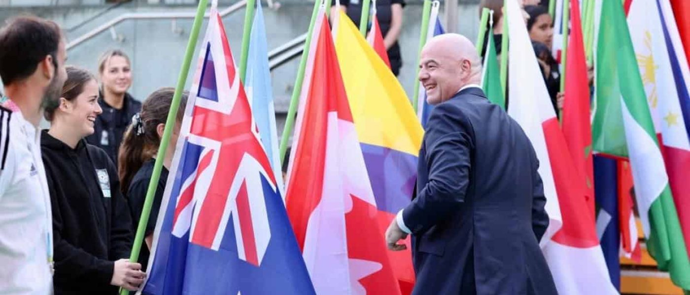 Gianni Infantino sonríe al pasar junto a una niña que sostiene la bandera de Nueva Zelanda en una ceremonia de la FIFA