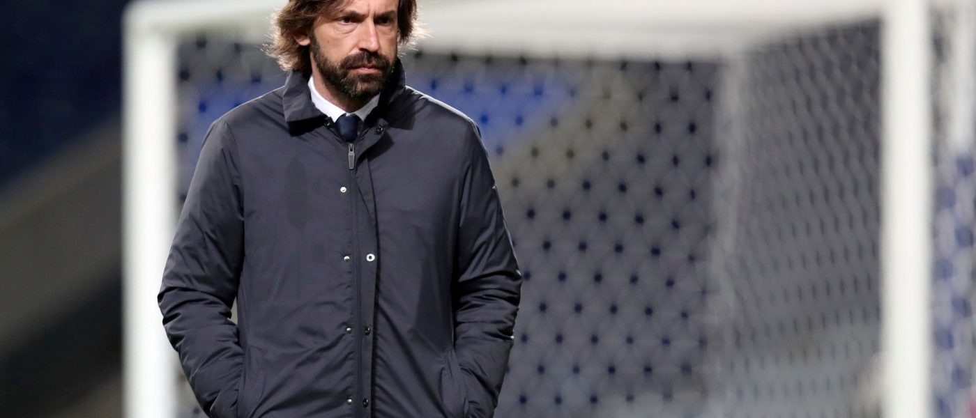 Andrea Pirlo, de campera oscura y con las manos en los bolsillos, camina por el costado del campo frente a un arco durante un partido