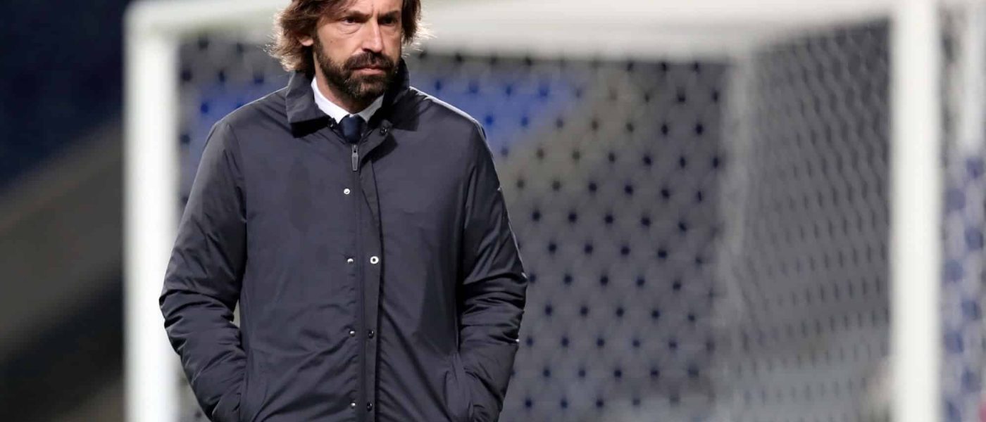 Andrea Pirlo, de campera oscura y con las manos en los bolsillos, camina por el costado del campo frente a un arco durante un partido