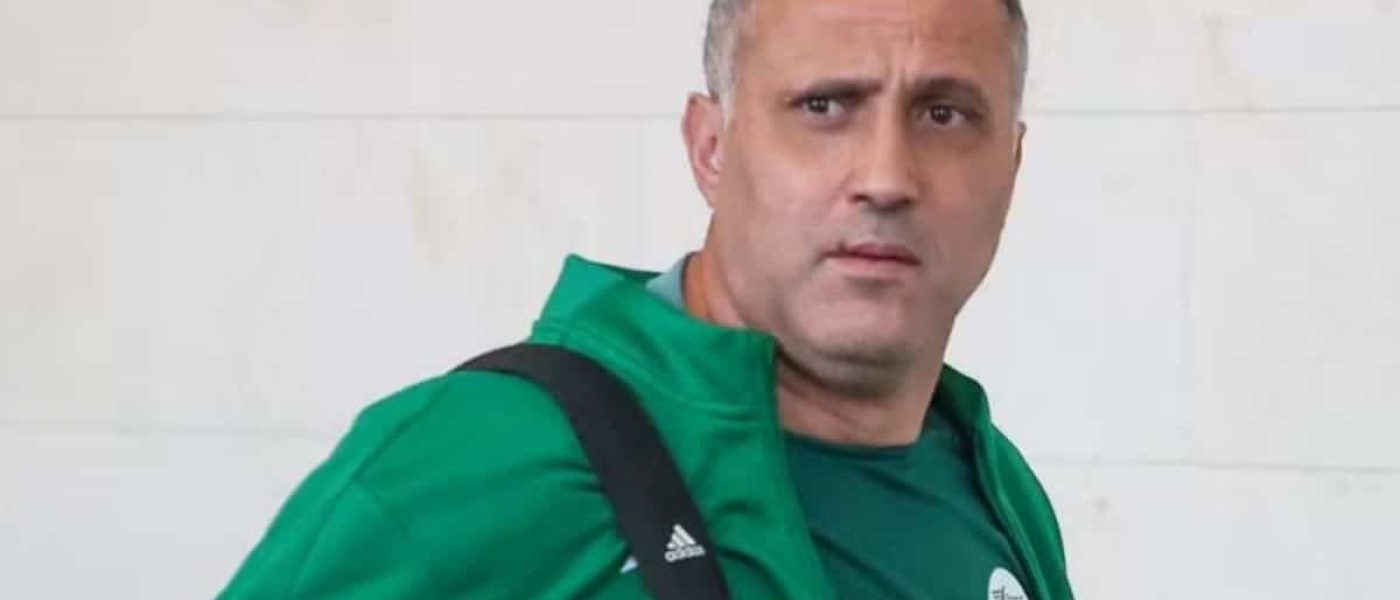 Brahim Hemdani con la campera verde de la selección argelina y un bolso al hombro, mirando a cámara frente a una pared blanca