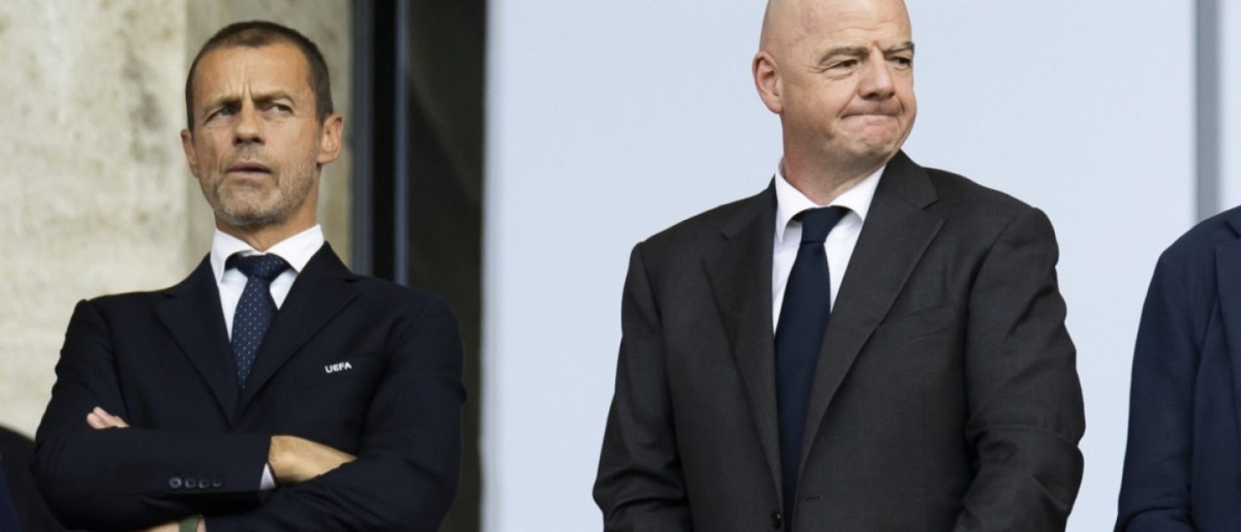 Aleksander Ceferin, de brazos cruzados, y Gianni Infantino, con gesto de incomodidad, de pie y de traje en un palco