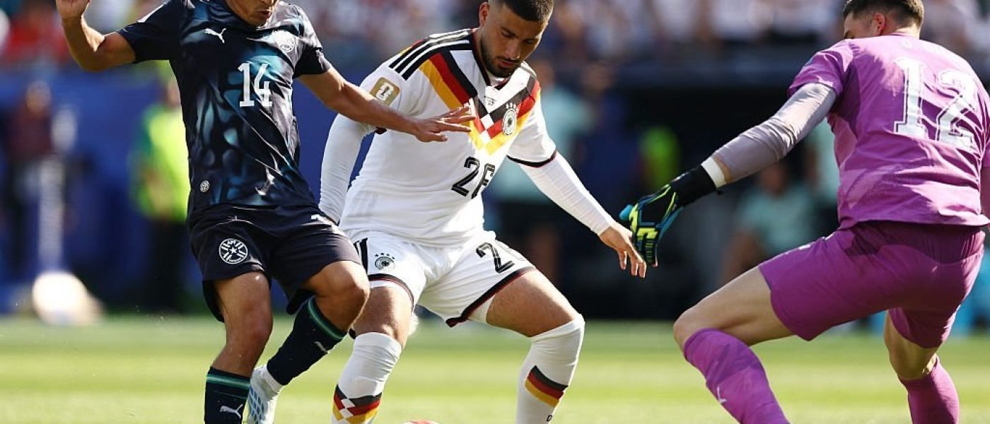 Un futbolista de Paraguay con la camiseta suplente azul disputa la pelota contra un jugador de Alemania y el arquero alemán durante el partido del Mundial 2026