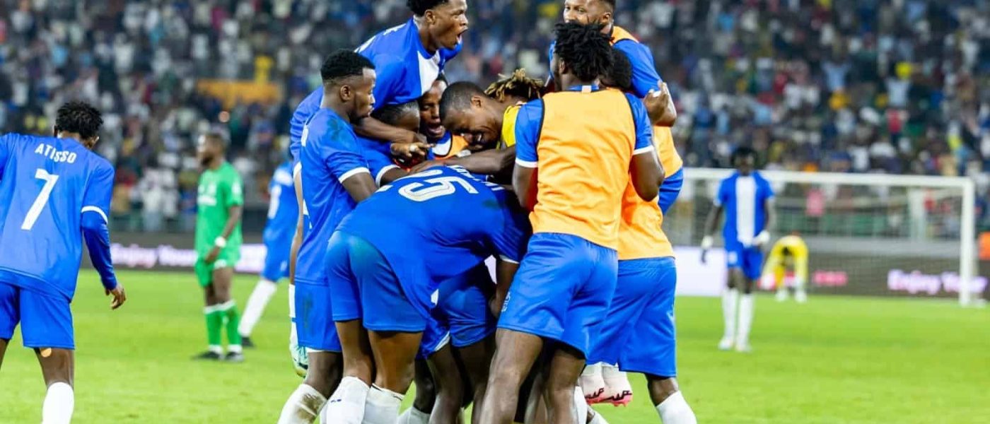 Jugadores de Rayon Sport se abrazan para festejar un gol en el Amahoro Stadium de Kigali, con las tribunas llenas y un futbolista de Gor Mahia de verde al fondo