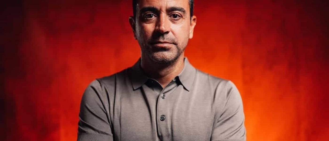 Xavi Hernández, de brazos cruzados y con remera gris, en un retrato sobre fondo rojo